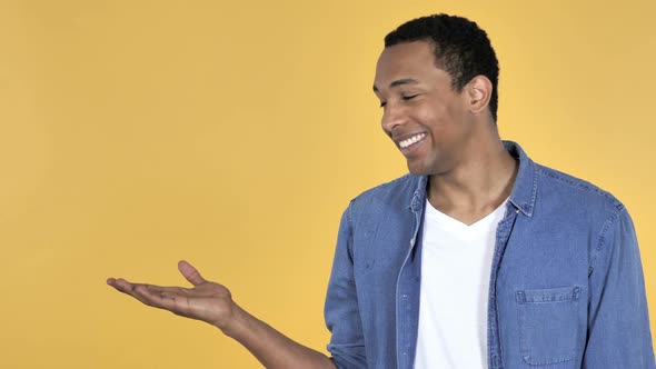 Young African Man Showing Product at Side Yellow Background alt