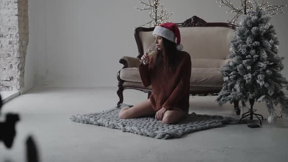 Portrait of Brunette Sitting on Carpet and Drinking Champagne