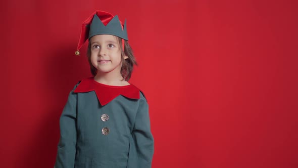 Boy Child in Dwarf Costume Stands on a Red Background Catching a Gift Box