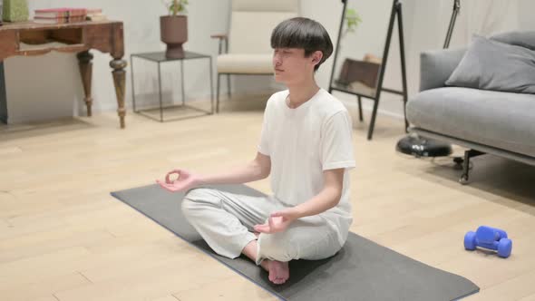 Asian Man Meditating on Yoga Mat at Home