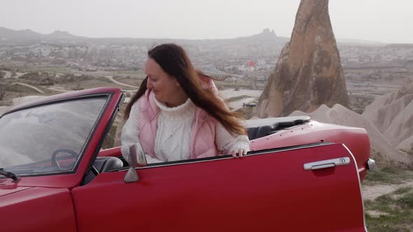 Brunette Woman Get Into Red Retro Cabrio in Valley of Cappadocia Close Car Door Hold Steering Wheel