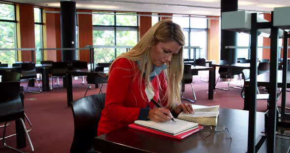 Mature student with reading glasses studying at library desk