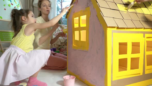 Young Family with Child Building and Painting Toy Cardboard House Together.