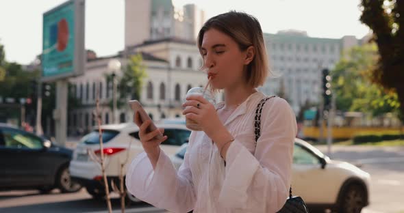 Woman Messaging By Mobile Phone Walking in a Summer City Drinking Cocktail