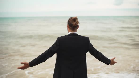 Businessman with Tied Hair Greeting Sea with Open Arms Backside to Camera Slowmotion