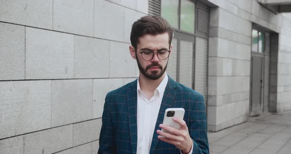 Confident Young Entrepreneur in Glasses Browsing Mobile Phone Internet During Office Break Walking