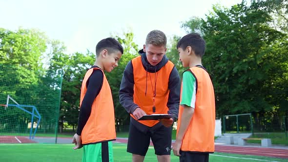 Soccer Trainer in Uniform which Explaining the Model of Game to His Smiling Teen Pupils