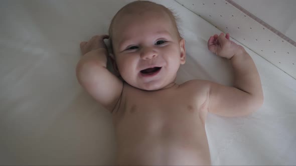 Playful Caucasian Baby Is Lying In Crib Laughing And Making Sounds