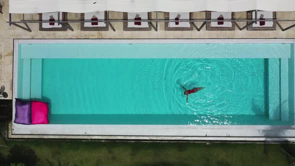 Female swimming face up at Shore Amora Canggu Hotel pool in Bali, Indonesia, Aerial top view shot