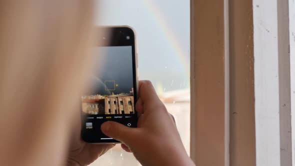 a Woman Photographs a Beautiful Rainbow on Her Phone on a Dark Blue Sky with Clouds and the Sun