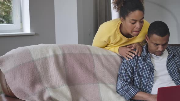 Positive Smiling African American Woman Supporting Man Messaging Online Sitting on Couch in Living