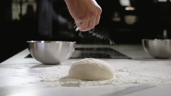 Baker in bakery makes morning dough for baking pizza sprinkles flour on dough