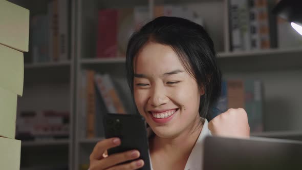 Close up front view of happy young Asian woman having new order from customer in smartphone