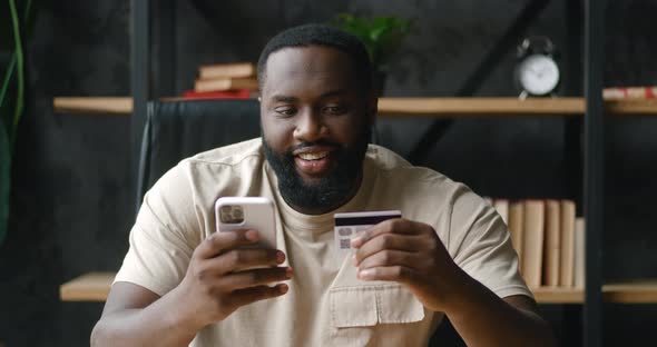 Happy African American Business Man Sitting at Office Desk Holding Credit Card and Mobile Phone to