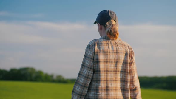 Rear View  Female Farmer Walks Among Wheat Fields on a Clear Summer Day