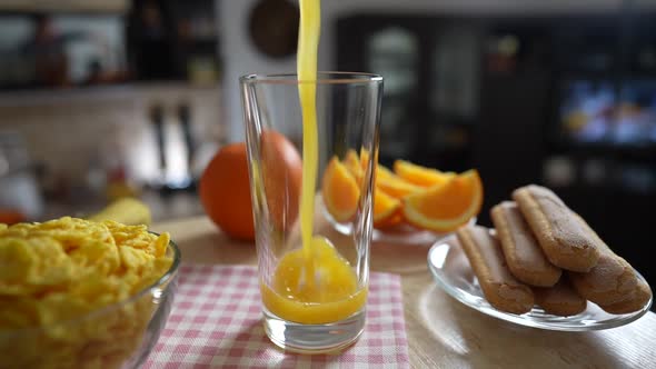 Pouring fresh orange juice into a glass on a rotating in kitchen, slow motion