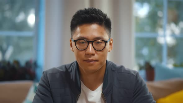 Portrait of Asian Man in Glasses Waving Hand Talking Online Via Video Call Sitting at Home