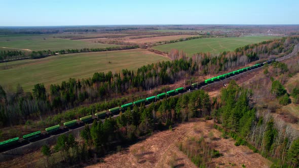 A Long Freight Train with Green Train Car Wagons Travels Among the Forest