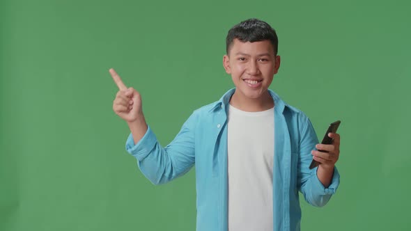 The Inspired Asian Boy Flipping Through The Phone With A Smile Pointing Side In The Green Screen