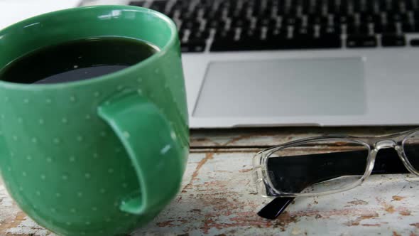 Coffee mug, laptop, spectacle on wooden plank