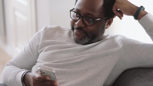 Smiling man watching TV and leafing tape on phone