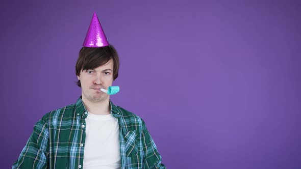 Young Man in Birthday Cone Cap Blowing Squeaker Frowns