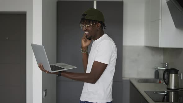 African American Man Working at Home in Kitchen Talking on Smartphone and Using Laptop