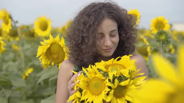 Portrait of Adorable Curly Playful Woman Looking at the Camera Smiling Standing in the Sunflower