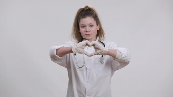 Caucasian Girl in Medical Uniform Showing Heart Shape with Hands Smiling Looking at Camera