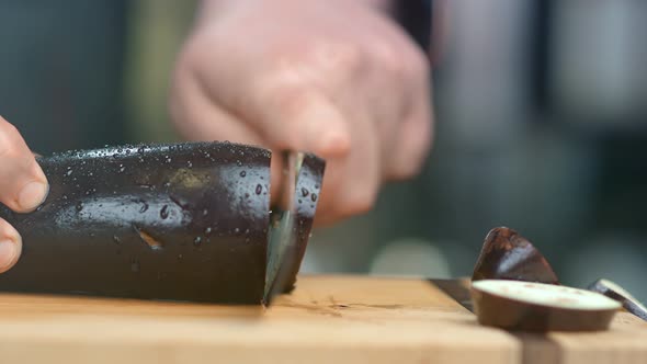 Professional Chef Hands Cuts Eggplant on Wooden Board Using Knife