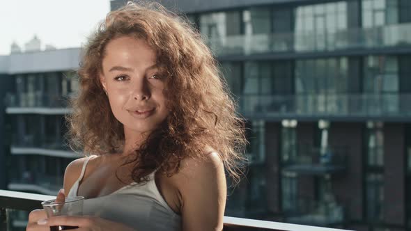 A Young Woman is Standing on the Balcony and Drinking Coffee