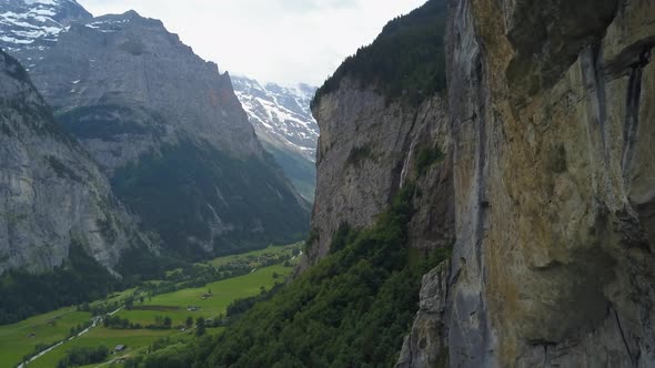 Aerial dolly out revealing Staubbach waterfall streaming down a steep rocky cliff near green valley,