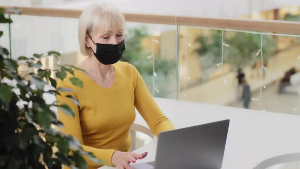 Happy Middle Aged Businesswoman in Medical Mask Sitting Working Typing Email on Laptop Using New
