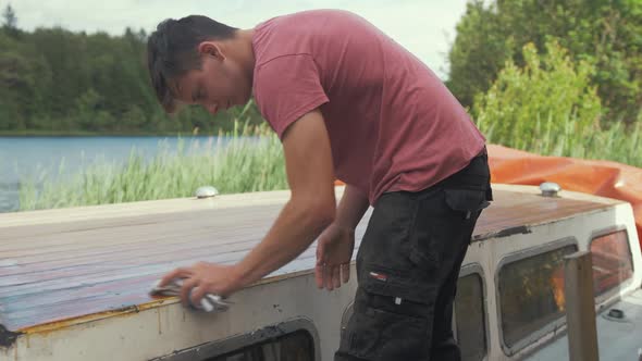 Young man wiping dust off boat roof planking after sanding planking. CLOSE UP.