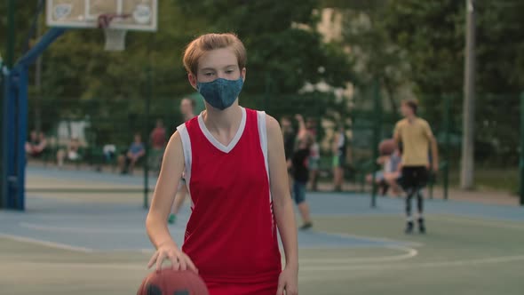 Portrait of a Girl in a Protective Mask Who Trains on the City Playground with a Basketball. A