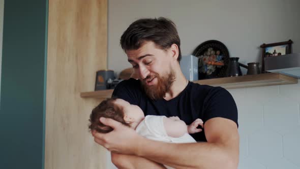 Handsome Bearded Dad Holding a Tiny Infant in His Hands and Showing Affection to Baby