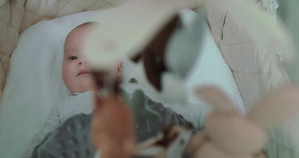 Little Smiling Baby Boy Lying in Bed with Moving Toys