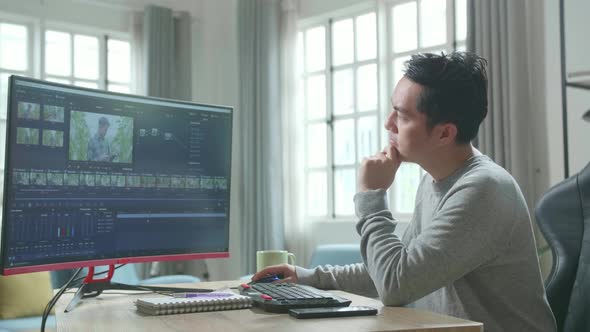 Asian Video Editor Man Thinking While Using Desktop Computer For Editing Video At Home