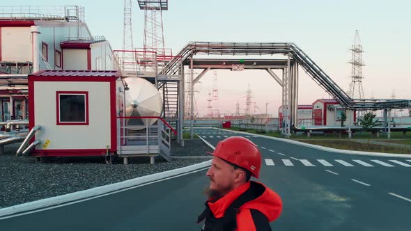 A Professional Factory Worker with a Beard Wearing a Red Hard Hat Inspects the Modern Industrial