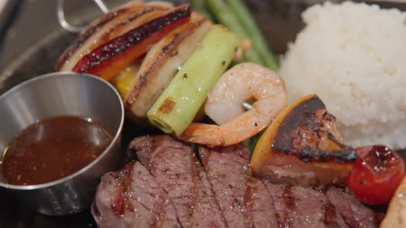 Beef Steak On Sizzling Plate With Rice And Seafood Skewer. - close up