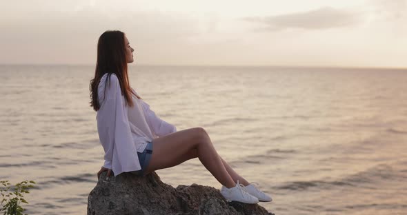 Young Woman Looks at the Sea Sunset Sitting on a Hill