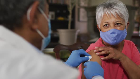 Male doctor visiting senior mixed race woman giving her vaccination