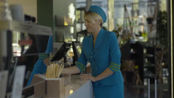 Portrait of Caucasian Stewardess in Uniform Buying Coffee-to-go and Leaving. Positive Smiling Young