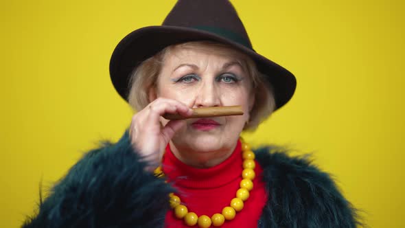 Wealthy Stylish Senior Woman in Elegant Hat Smelling Expensive Cigar