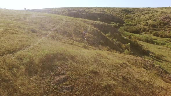 Flyback Drone Shot of Tourists Walking Through Rocky Cross Country with Yellow and Green Grass