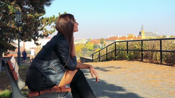 Young Beautiful Woman Sits on the Bench in Park and Relax (Looks Around)