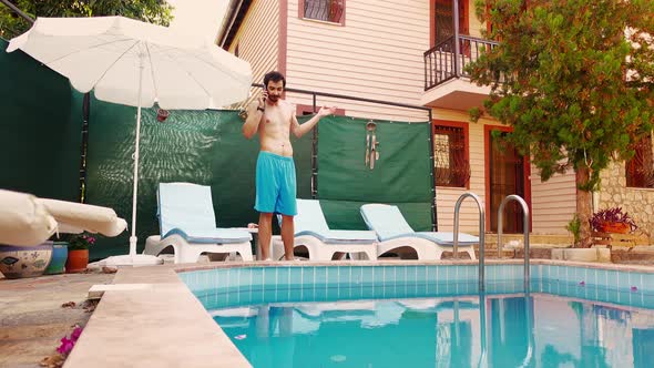 Young Man in Swimwear is Standing Near Swimming Pool on Villa and Talking on Smartphone