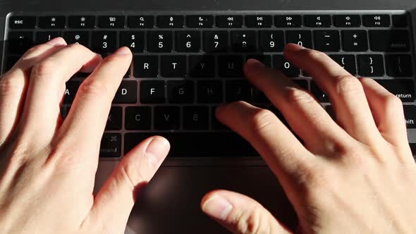 Static overhead shot of Caucasian person typing on a laptop keyboard on desk.