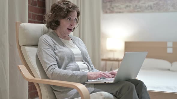 Surprised Old Woman Celebrating Success on Laptop on Sofa