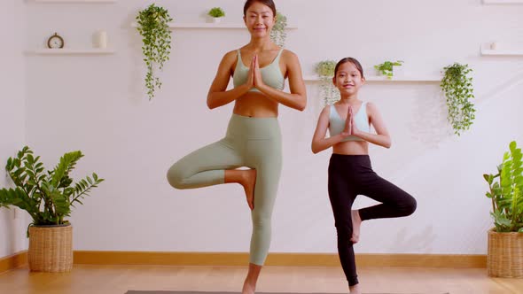 Healthy couple mom and little girl doing yoga one leg stand on yoga mat at home.Mother and female da